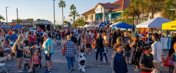 Families in Halloween costumes walking past vendor tents at a fall Beach-O-Ween event in Pensacola