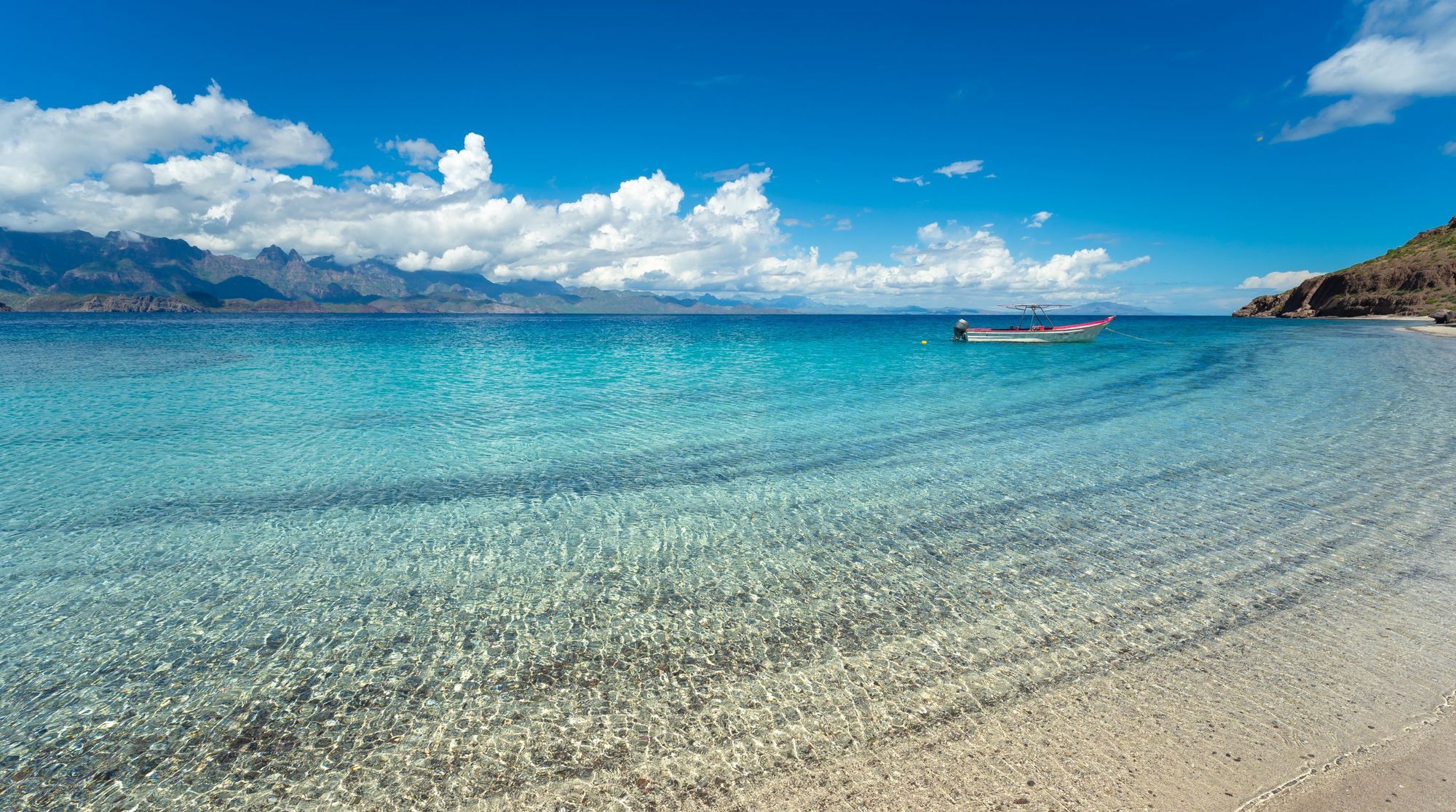Clear shallow water lapping a white sand beach on Isla del Carmen, with a fishing boat anchored offshore
