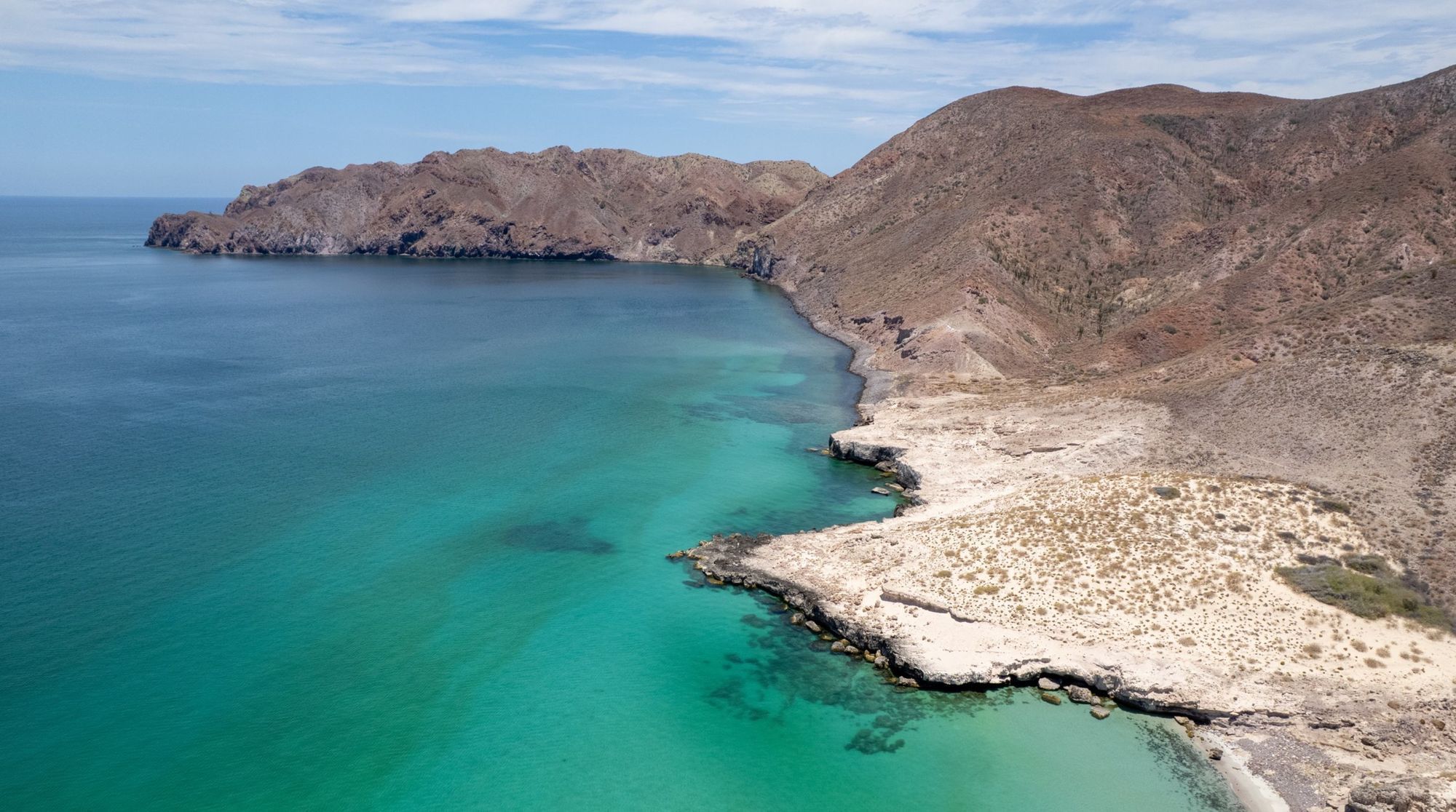 Aerial view of Isla Montserrat coastline with desert terrain meeting turquoise water