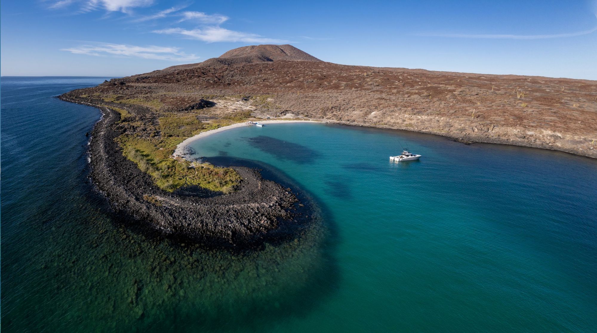 Aerial view of Isla Coronado with a curved rocky shoreline, white sand beach, and a boat anchored in the bay